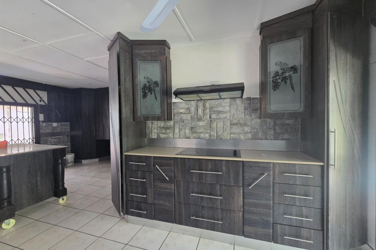 A functional kitchen featuring dark wood-grain cabinetry, a built-in hob with extractor fan, and tiled flooring, offering a practical layout for culinary activities.