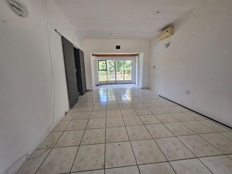 An empty, open-plan living area featuring tiled flooring, a wall-mounted air conditioner, and a sliding door leading to the exterior.