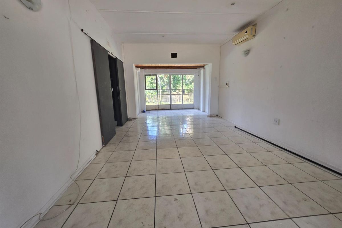 An empty, open-plan living area featuring tiled flooring, a wall-mounted air conditioner, and a sliding door leading to the exterior.