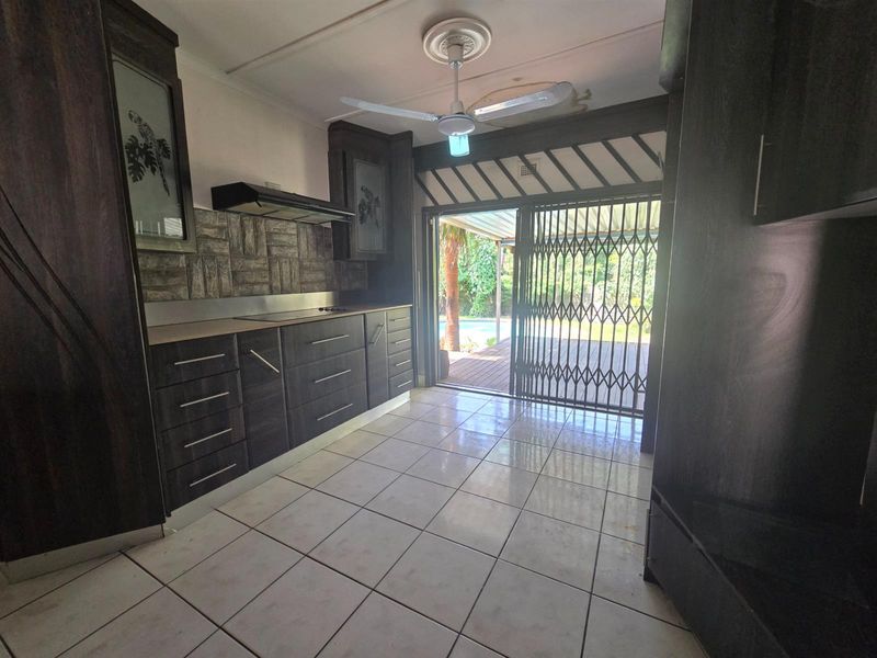 A functional kitchen featuring dark built-in cabinetry, tiled flooring, and direct access to the outdoor patio and pool area through a security gate.