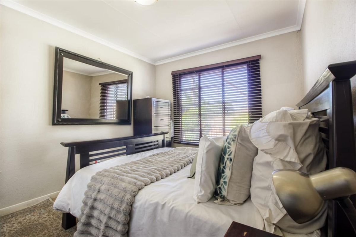 A well-maintained bedroom featuring neutral wall tones, coved ceilings, and fitted venetian blinds.