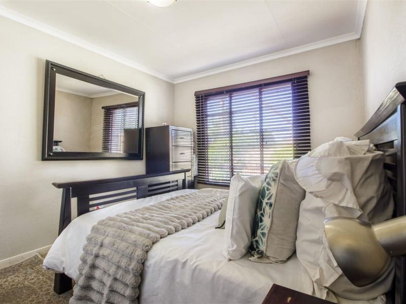 A well-maintained bedroom featuring neutral wall tones, coved ceilings, and fitted venetian blinds.