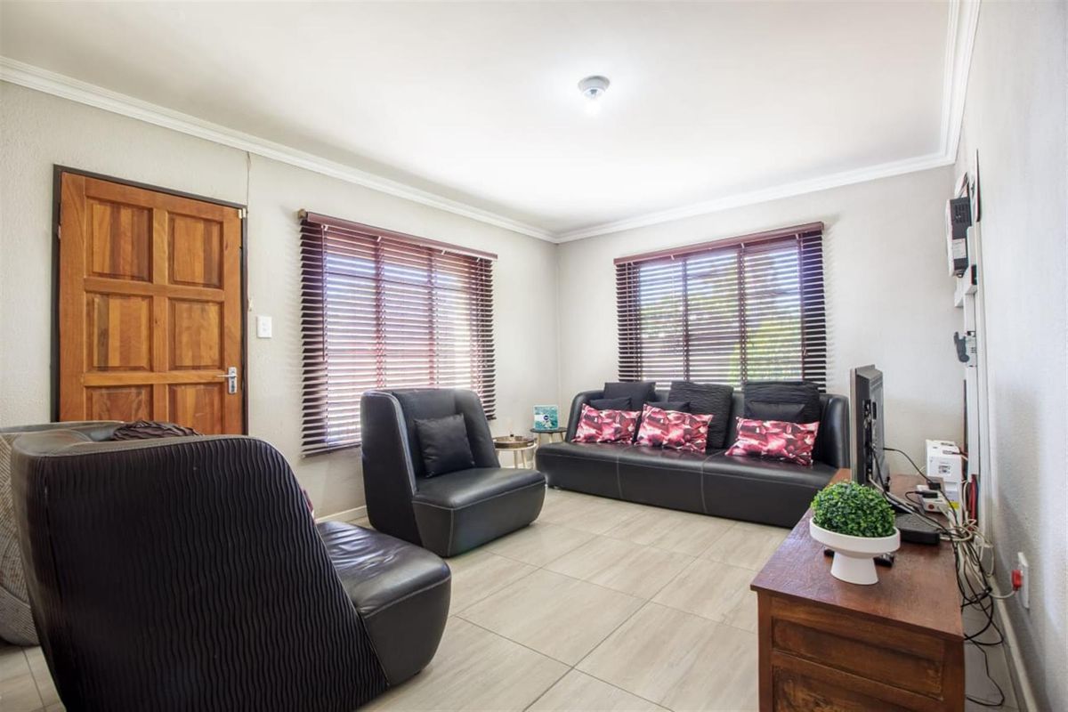 A living room featuring tiled flooring, wooden door, and venetian blinds, providing a functional and neutral space for relaxation.