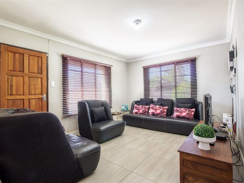 A living room featuring tiled flooring, wooden door, and venetian blinds, providing a functional and neutral space for relaxation.
