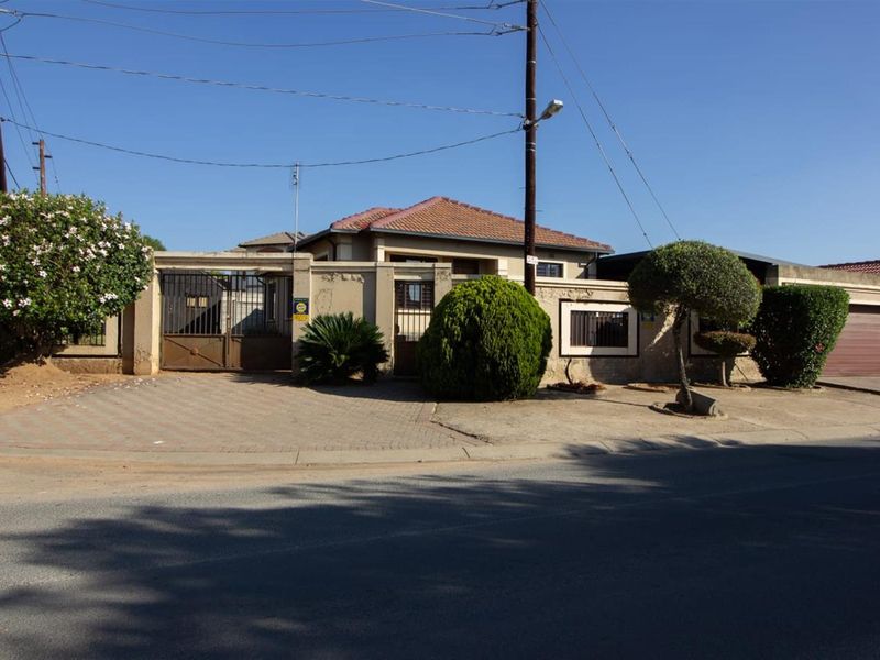 Front elevation of the property featuring a paved driveway, secure metal gate, perimeter wall, and attached garage.