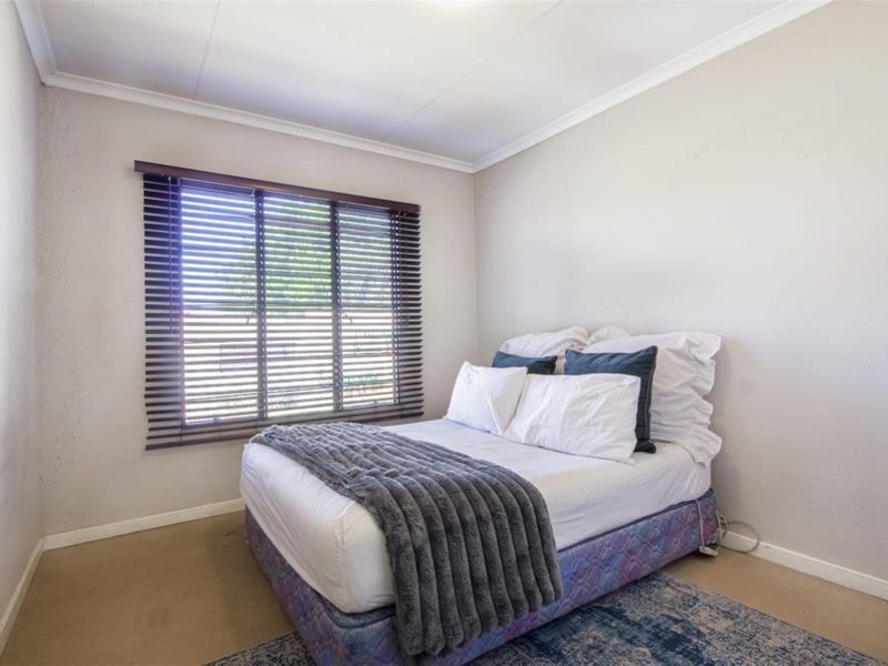 A neutrally painted bedroom featuring a window with fitted venetian blinds and classic cove cornicing.