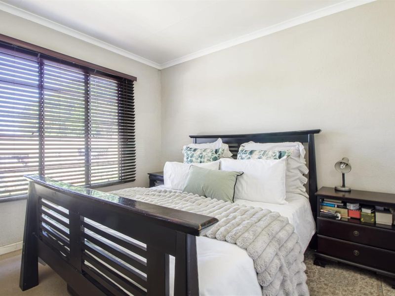 A comfortable bedroom featuring carpeted flooring, neutral walls, and a window fitted with dark venetian blinds.