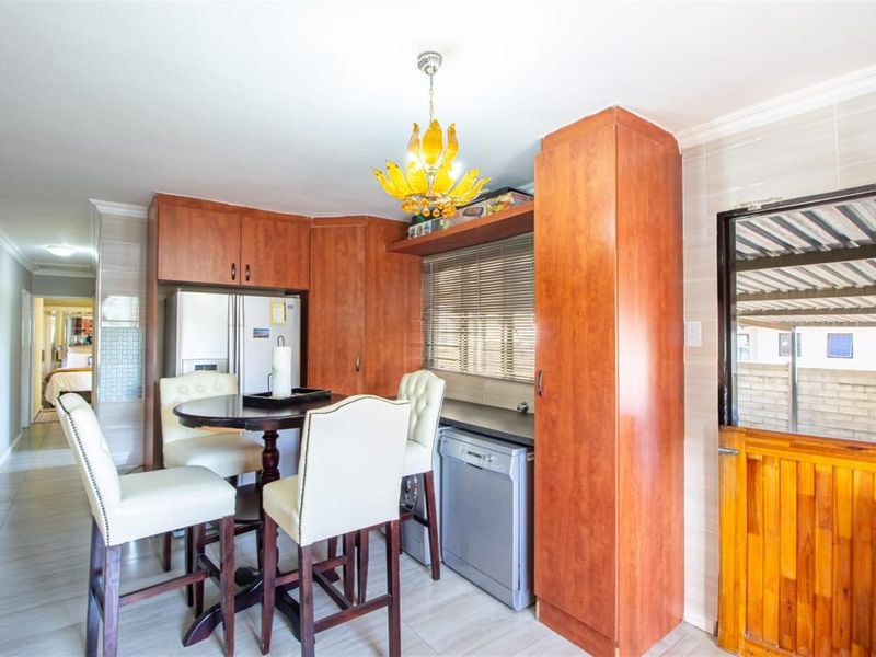 A functional kitchen area featuring wood-finish cabinetry, tiled flooring, and a stable door leading to the exterior, with an integrated dishwasher and dining space.