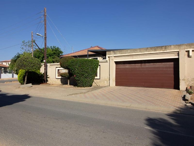 Street-facing view of the property featuring a single garage door, paved driveway, and boundary wall with visible exterior maintenance requirements.