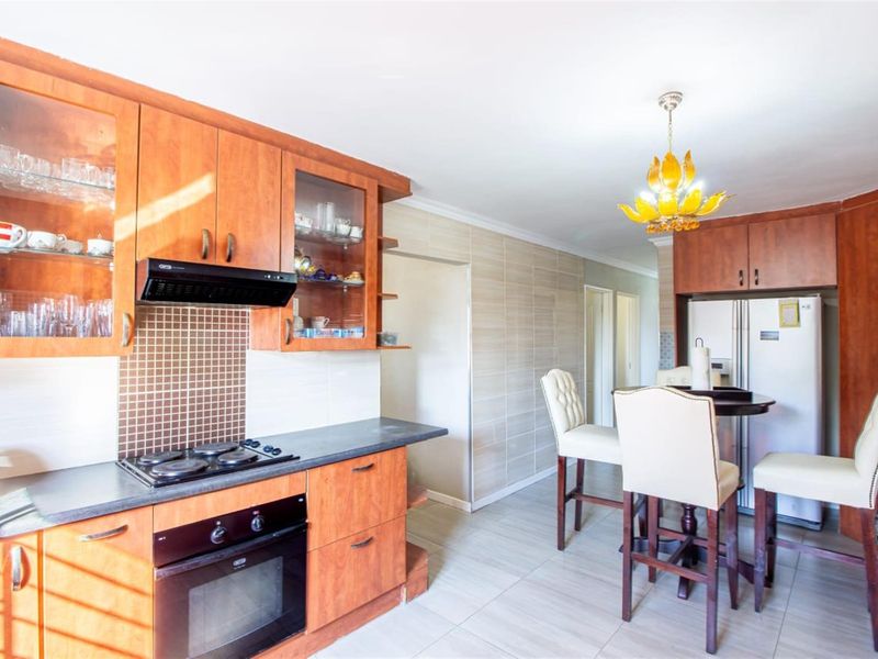 A functional kitchen featuring wood-finish cabinetry, dark countertops, integrated appliances, and tiled splashbacks, offering a practical layout for daily cooking and dining.