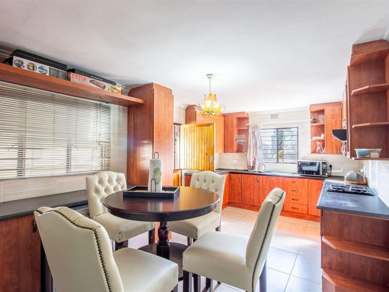 A functional kitchen featuring warm-toned wooden cabinetry, dark laminate countertops, a built-in hob, and tiled flooring, offering a practical layout for daily use.