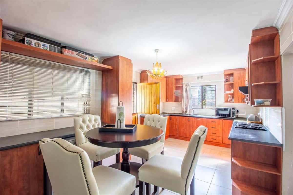 A functional kitchen featuring warm-toned wooden cabinetry, dark laminate countertops, a built-in hob, and tiled flooring, offering a practical layout for daily use.