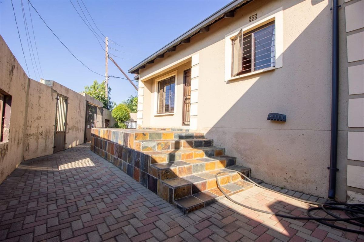 Rear exterior view featuring a paved courtyard, a tiled staircase leading to the entrance, and secure boundary walls.