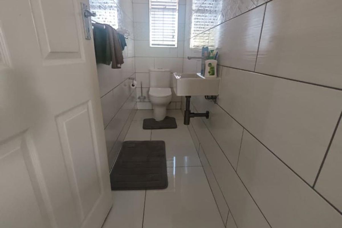 A compact, modern bathroom featuring white wall tiles with decorative accents, a wall-mounted basin, and a standard toilet.
