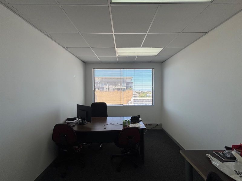 A functional office space featuring a suspended ceiling, recessed lighting, carpeted flooring, and a large window providing natural light and exterior views.