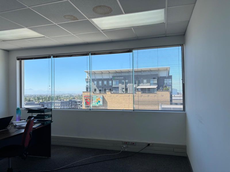 A functional office space featuring large windows with city views, carpeted flooring, and a suspended ceiling with integrated lighting.