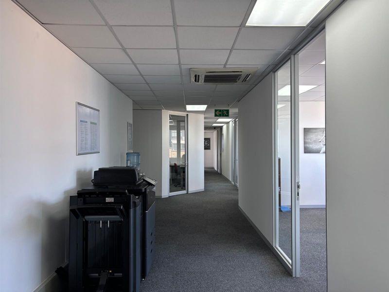 A clean, professional office hallway featuring suspended ceilings, recessed lighting, integrated air conditioning, and glass partition walls leading to private office spaces.