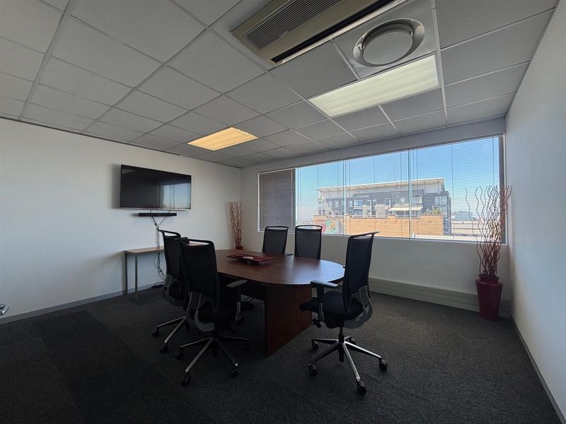A professional office meeting room featuring a suspended ceiling, recessed lighting, central air conditioning, and large windows with venetian blinds.