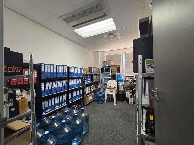 A functional utility or storage room featuring a suspended ceiling, integrated air conditioning, and carpeted flooring, currently utilized for document and supply storage.