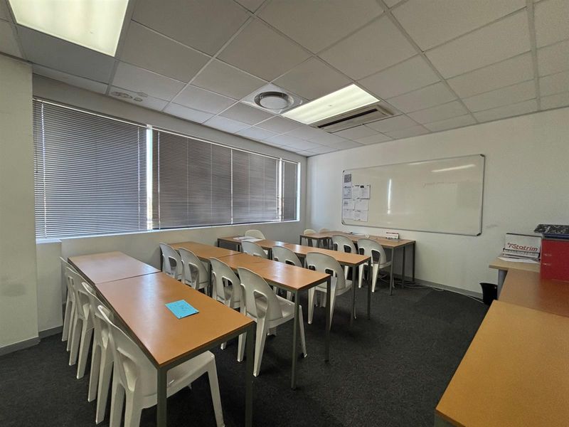 A functional office space featuring a suspended ceiling, recessed lighting, venetian blinds, and a wall-mounted whiteboard, suitable for a training or meeting room setup.