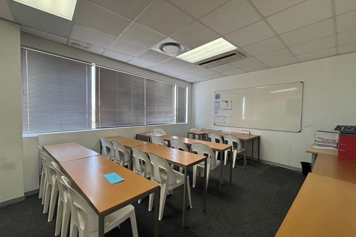 A functional office space featuring a suspended ceiling, recessed lighting, venetian blinds, and a wall-mounted whiteboard, suitable for a training or meeting room setup.