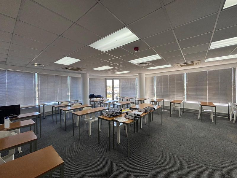 Spacious office area featuring a suspended ceiling, recessed lighting, carpeted flooring, and large windows with venetian blinds, providing ample natural light.