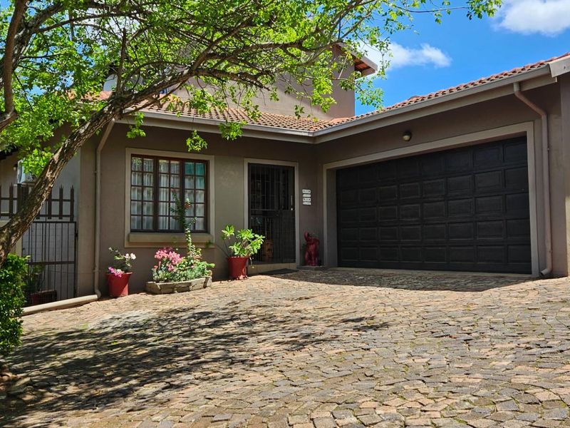 Front exterior view of the house featuring a cobblestone driveway, double garage, and secure entrance with established trees.