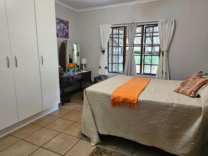 A functional bedroom featuring built-in cupboards, tiled flooring, and natural light through casement windows.