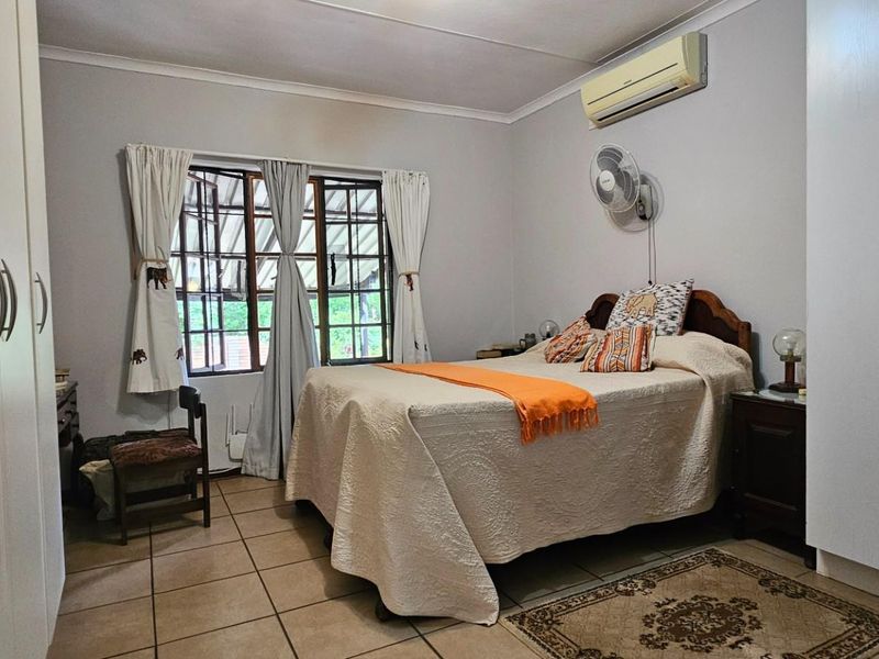 A functional bedroom featuring built-in cupboards, tiled flooring, and a wall-mounted air conditioning unit.