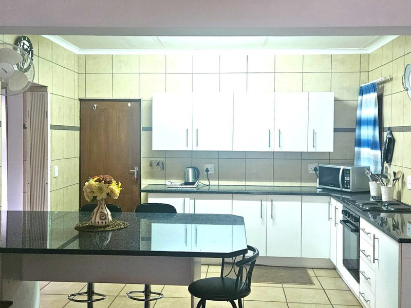 A functional kitchen featuring granite countertops, a breakfast bar, built-in oven, hob, and ample white cabinetry with tiled wall finishes.