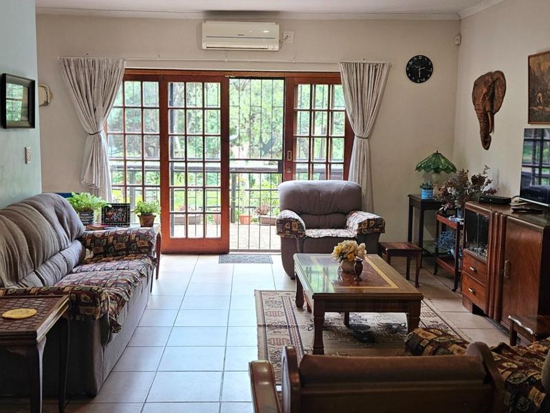 A comfortable living room featuring ceramic floor tiles, a wall-mounted air conditioning unit, and wooden framed glass sliding doors leading to the outdoors.
