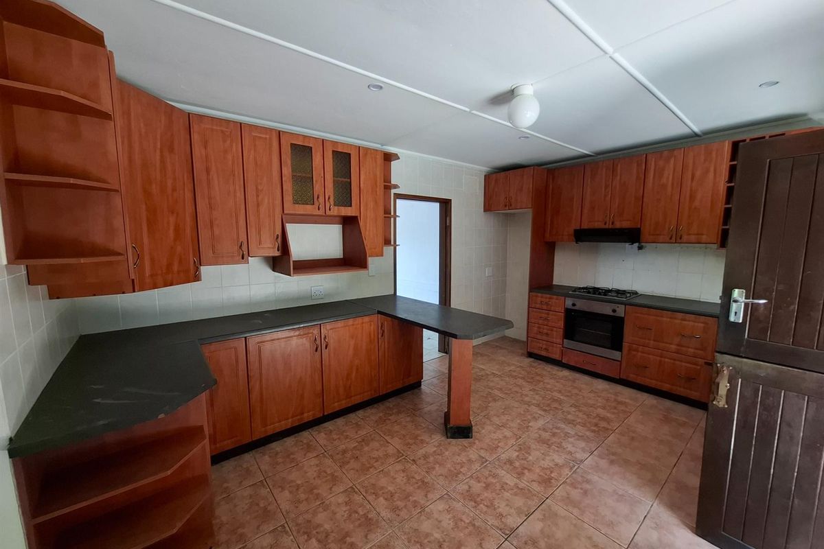 A functional kitchen featuring wood-finish cabinetry, dark countertops, a built-in oven and hob, and tiled flooring throughout.