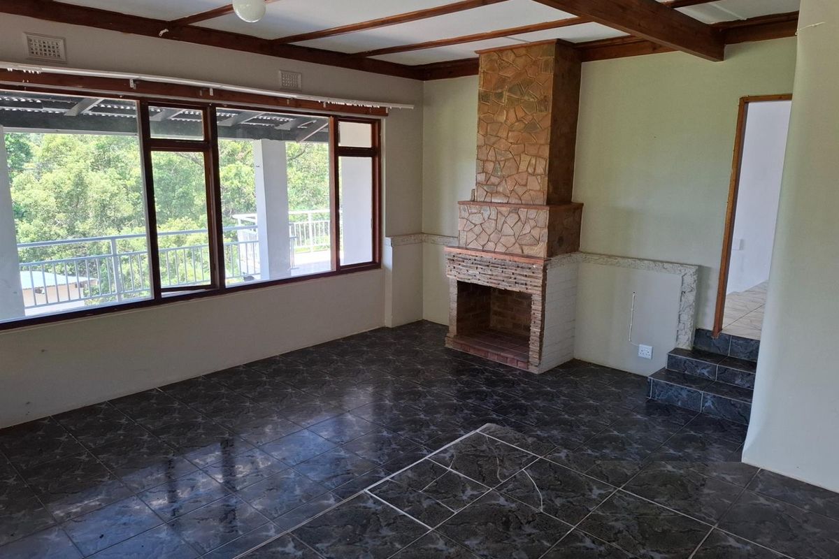 Spacious living room featuring a prominent stone fireplace, exposed timber ceiling beams, and large windows providing natural light and access to the outdoor area.