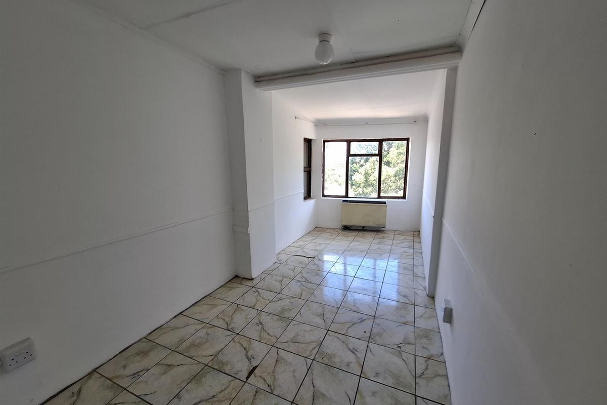 An empty, rectangular room featuring tiled flooring, a window with natural light, and a wall-mounted air conditioning unit.