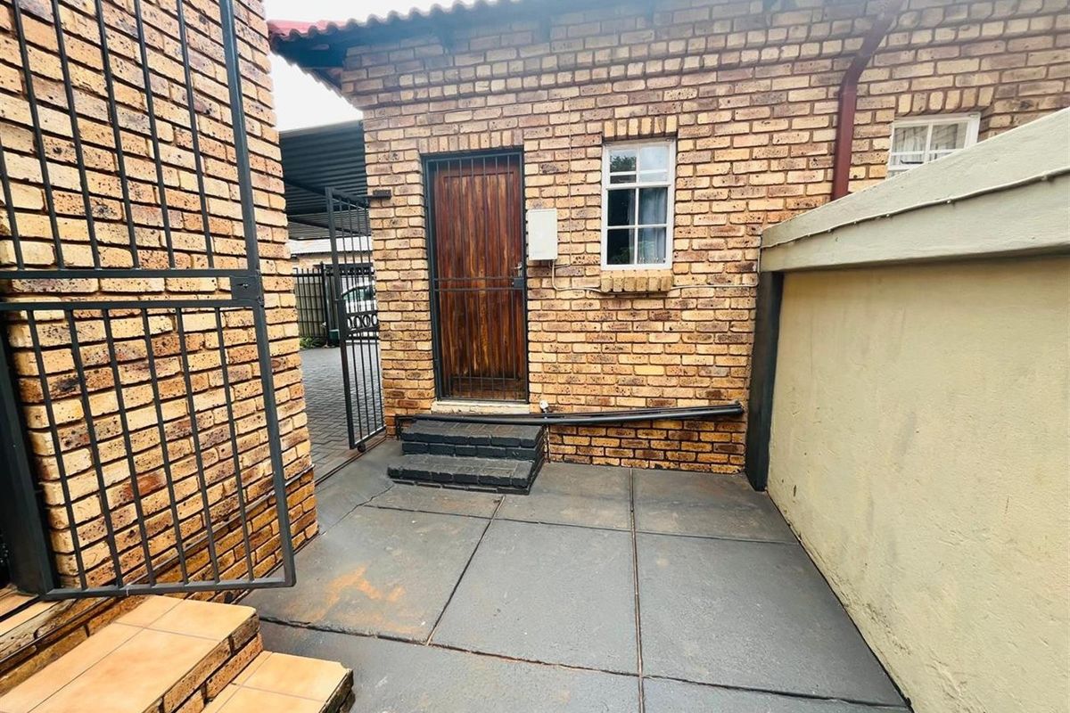 A rear exterior view showing a face brick facade, security gate, and paved patio area with concrete steps.