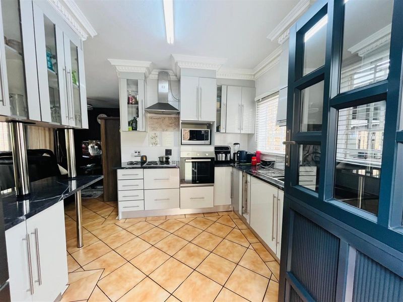 A well-maintained kitchen featuring white cabinetry, dark countertops, built-in appliances, and tiled flooring with decorative cornice detailing.