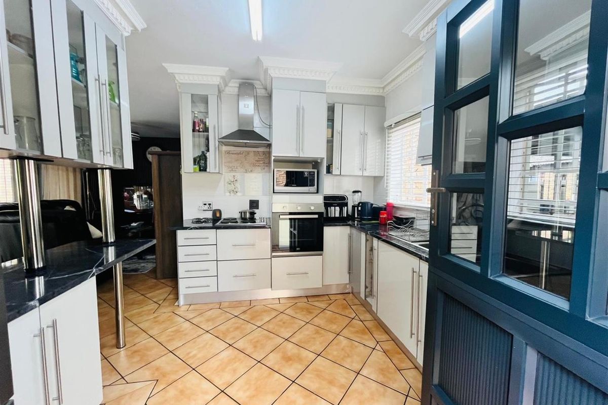 A well-maintained kitchen featuring white cabinetry, dark countertops, built-in appliances, and tiled flooring with decorative cornice detailing.