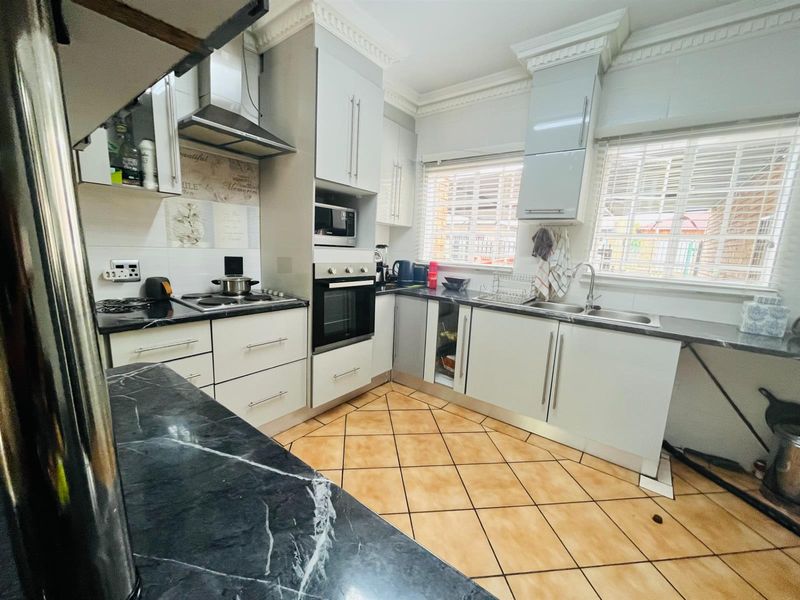 Functional kitchen featuring built-in oven, extractor fan, marble-look countertops, and tiled flooring, offering a practical layout with ample storage space.