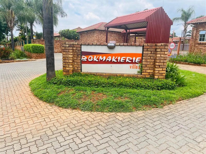 The entrance to Bokmakierie Villas featuring a brick boundary wall, signage, and paved driveway access.