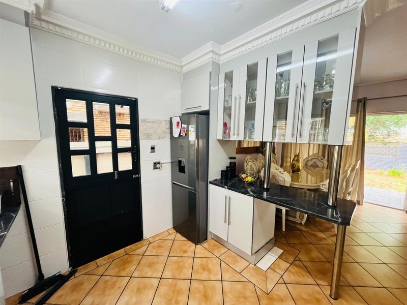 A functional kitchen featuring white cabinetry, glass-fronted display cupboards, a dark marble-look countertop, and tiled flooring with decorative ceiling cornicing.
