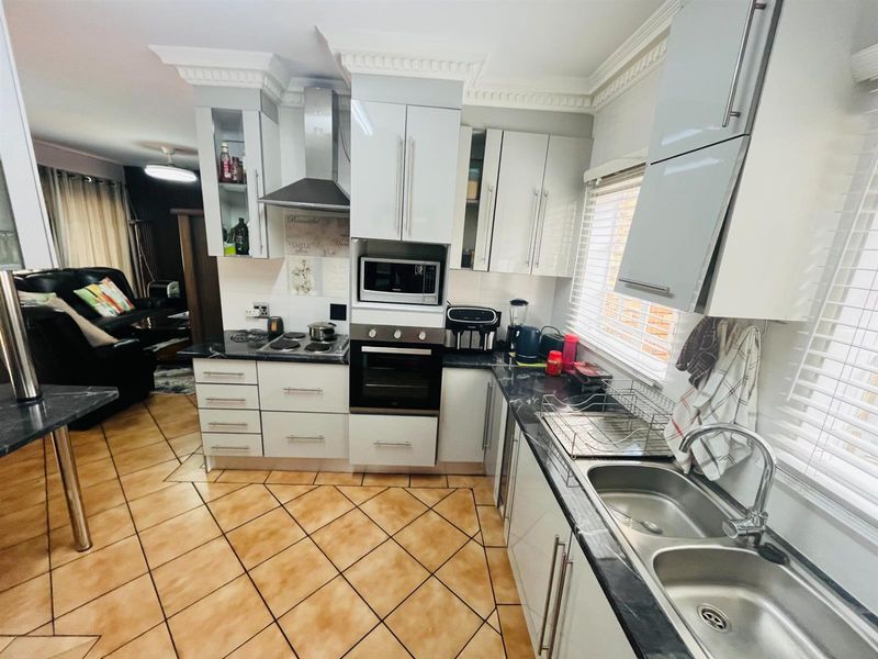 A functional kitchen featuring white cabinetry, dark laminate countertops, built-in appliances, and tiled flooring, seamlessly connected to the adjacent living area.