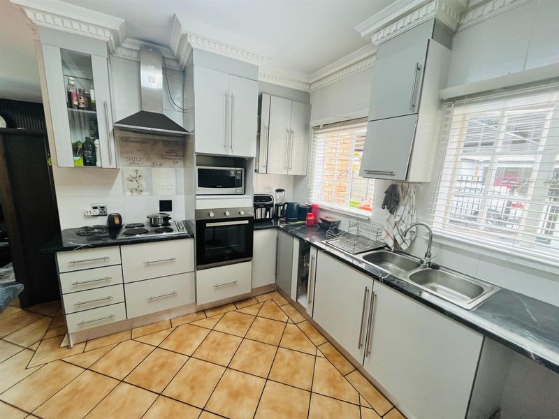 A functional kitchen featuring white cabinetry, dark countertops, built-in oven and hob, double sink, and tiled flooring with decorative crown molding.