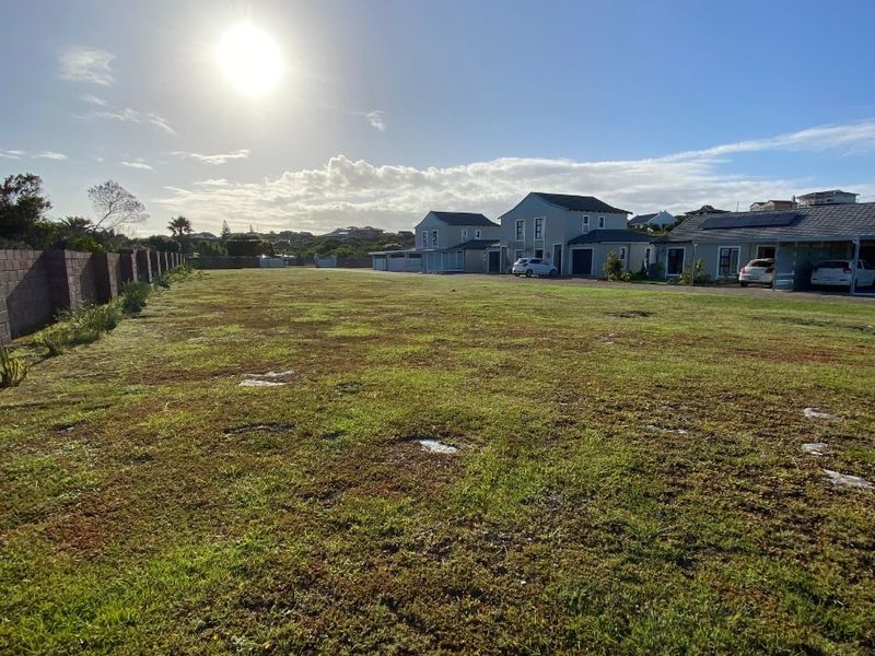 A wide, level residential vacant plot featuring a grass lawn and boundary wall, situated in a developed neighbourhood.