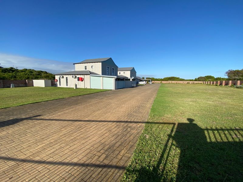 A wide view of the property frontage featuring a long paved driveway, expansive lawn, and boundary wall surrounding the residential building.