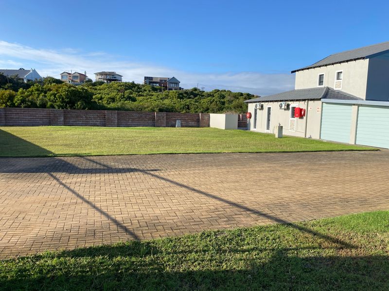 A spacious residential property featuring a large paved driveway, well-maintained lawn, and a brick boundary wall, adjacent to a multi-car garage structure.