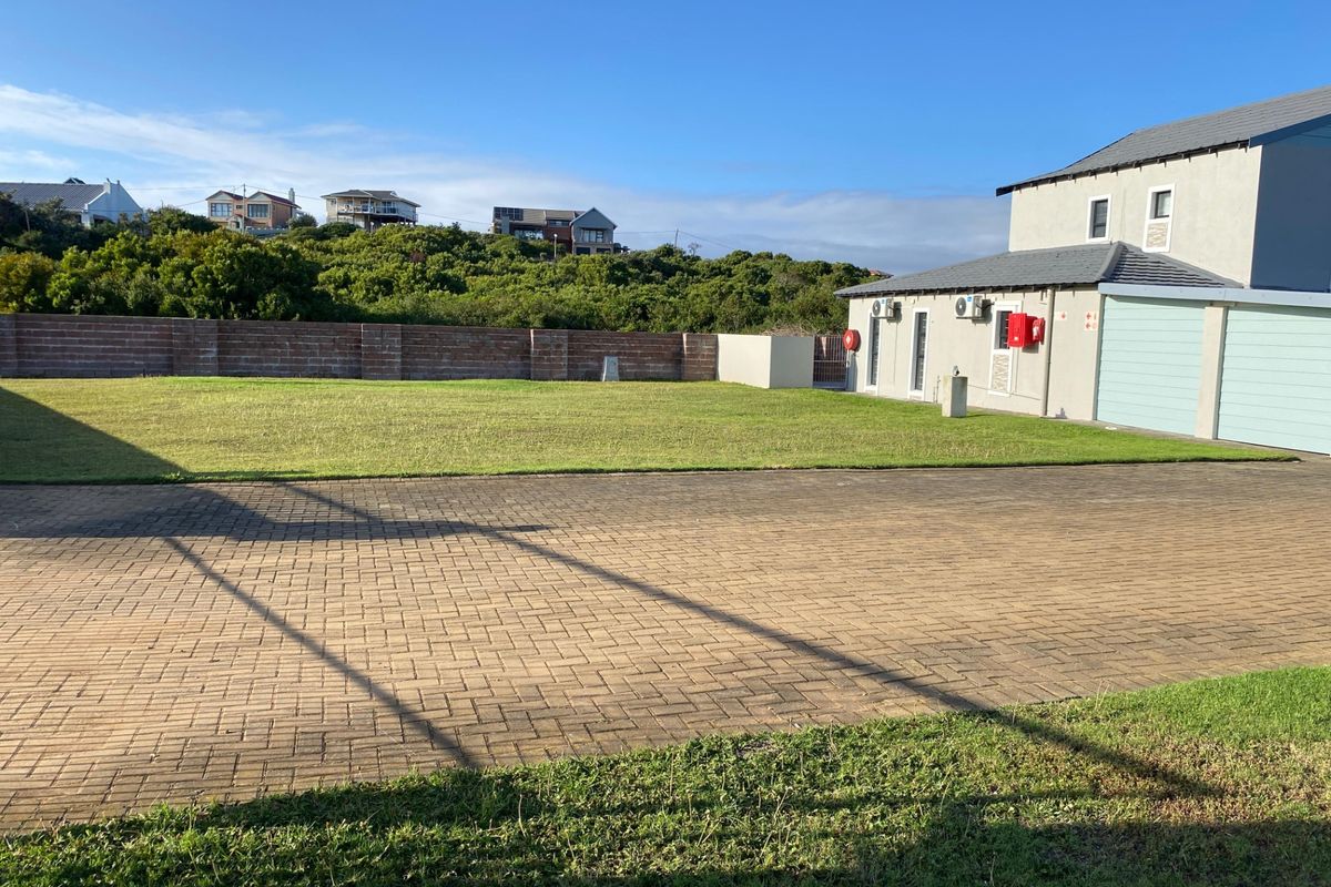 A spacious residential property featuring a large paved driveway, well-maintained lawn, and a brick boundary wall, adjacent to a multi-car garage structure.