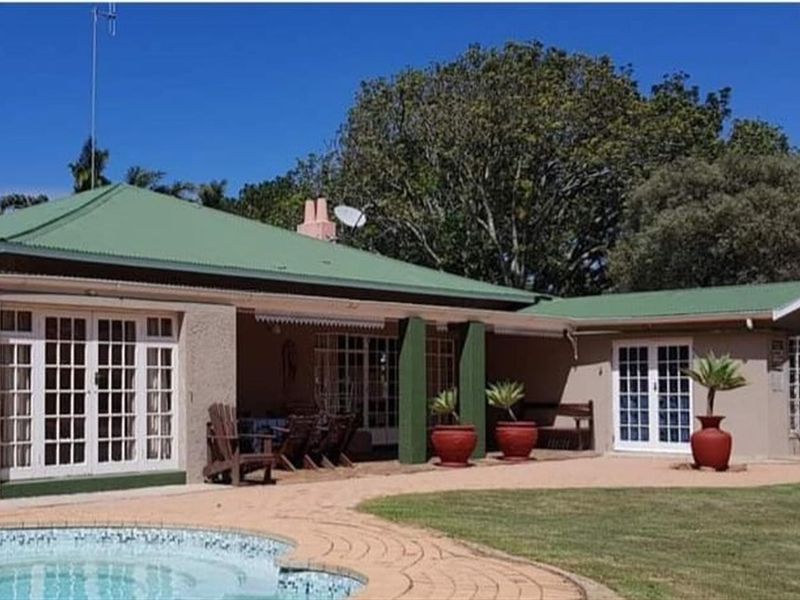 A rear view of the farmhouse featuring a covered patio area, swimming pool, and well-maintained garden surroundings.
