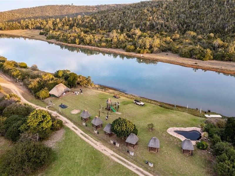 Aerial view of a riverside farm property featuring multiple thatched-roof structures, a small pool, and expansive landscaped grounds along the water's edge.