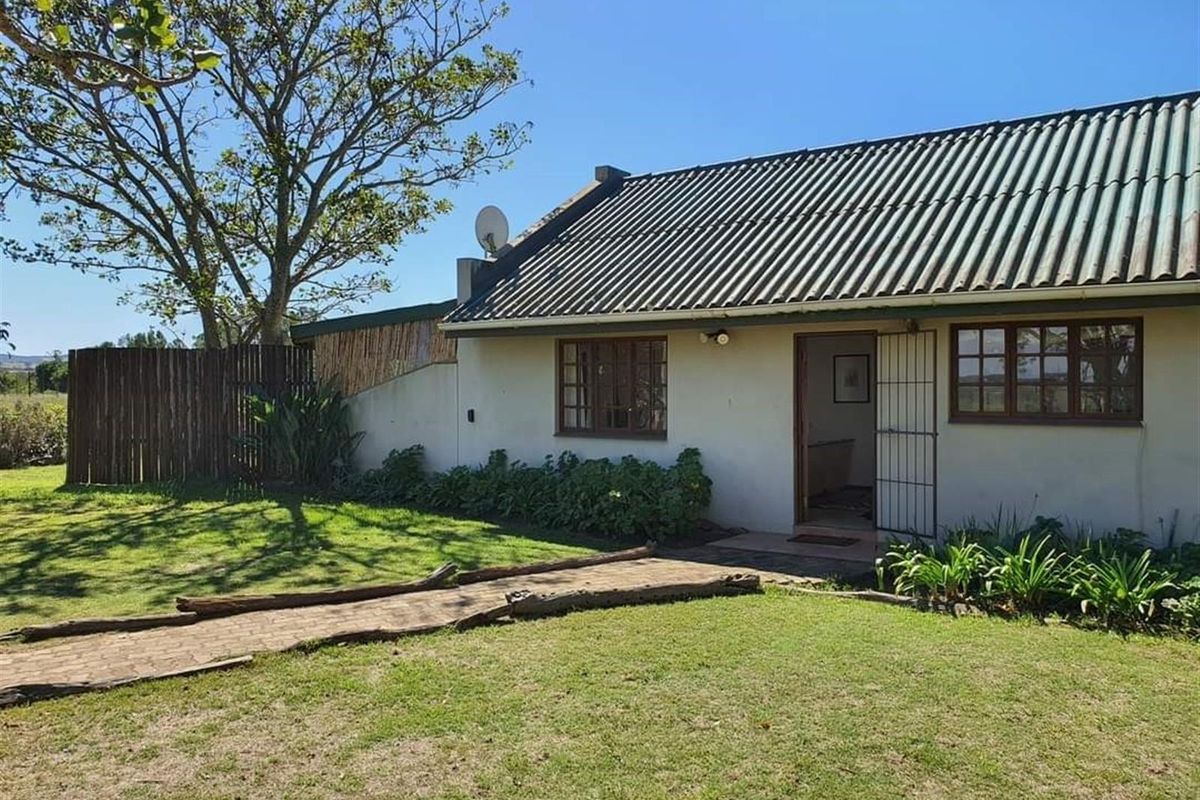 Rear view of the farm cottage featuring a corrugated roof, timber-framed windows, and a garden pathway leading to the entrance.