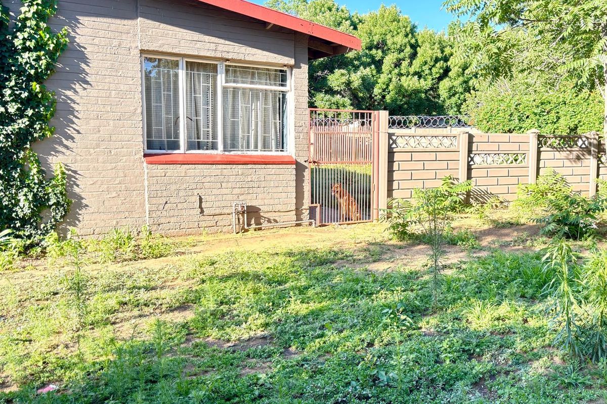 Rear exterior view of the house featuring brick walls, metal security gate, and an overgrown garden area.